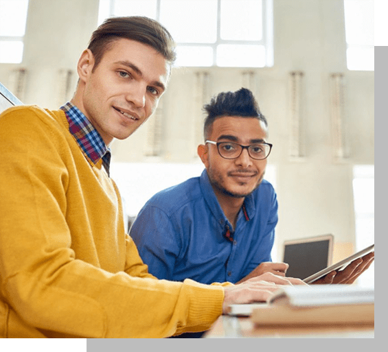 Two men sitting at a table with laptops.